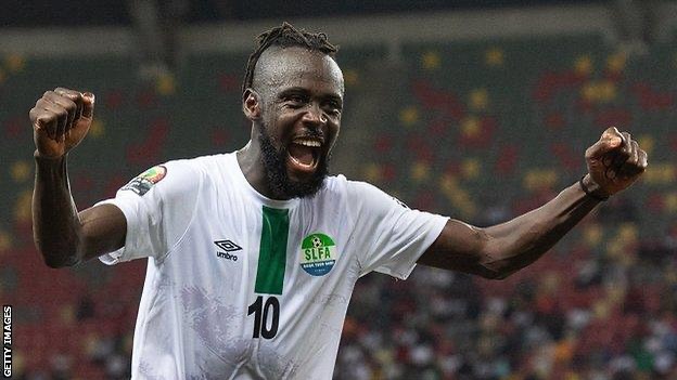 Kei Kamara celebrates after scoring a goal for Sierra Leone’s Leone Stars, raising his hands to the sky while wearing the Green, White and Blue national team jersey